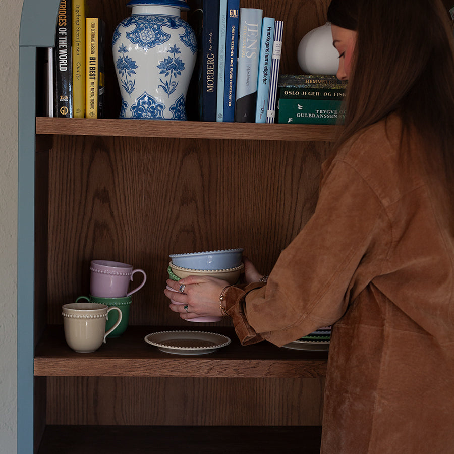 Kvinne pynter en hylle med fargerike kopper og tallerkener, perfekt for å inspirere til ideer til vertinnegave.