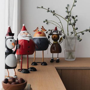 Christiania 1739 Julekolleksjon Figur Reinsdyr 18cm, reinsdyrfigur står sammen med flere juledekorasjoner, inkludert en pingvin og en julenisse, på et stilrent bord.