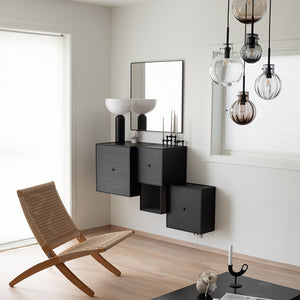Moderne stue med Hadeland Glassverk krystallkule taklampe over et stilrent svart møbel, kombinert med en minimalistisk stol.