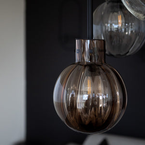 Nærbilde av Hadeland Glassverk krystallkule pendellampe i røykfarget glass, designet for å skape atmosfære i interiøret.