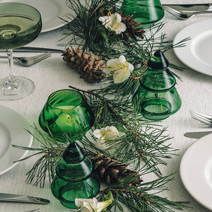 Dekorativ borddekorasjon med Hadeland Glassverk Gran Juletre 9,8 cm i vintergrønn glass omgitt av naturlige elementer.