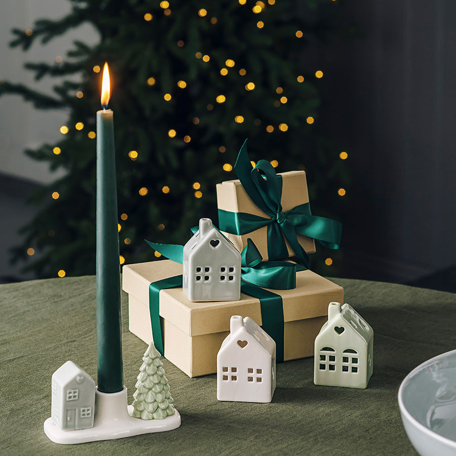 Porsgrunds Porselænsfabrik PP Jul Mini Hus med LED lys i sett, dekorative porselenshus med juletema, plassert ved siden av gaver og en grønn lysestake på et bord