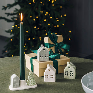 Porsgrunds Porselænsfabrik PP Jul Mini Hus med LED lys i sett, dekorative porselenshus med juletema, plassert ved siden av gaver og en grønn lysestake på et bord