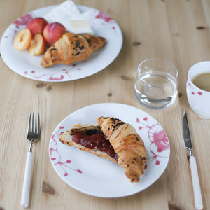 Porsgrund Porselænsfabrik Maxistrå Tallerken 22 cm Rosa, tallerken med croissant og frukt på bordet, som viser bruken av tallerkenen til frokost.