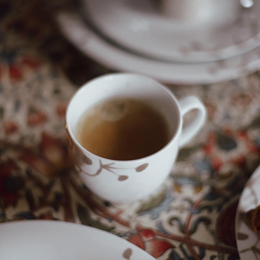 Porsgrund Porselænsfabrik Maxistrå Krus 35cl Nomi Beige fylt med te, satt på et fargerikt bord, som viser krusets tidløse eleganse.