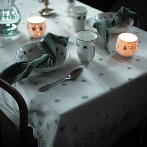 Wik & Walsøe damaskduk i hvit med julemotiver, dekket med dekorative lys og servise til en festlig middag.