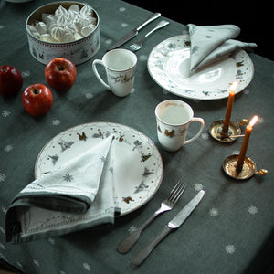 Bordet dekket med Julemorgen Damaskduk i grønn fra WIK & WALSØE, sammen med tallerkener, glass og julepynt, perfekt til festlig samvær.