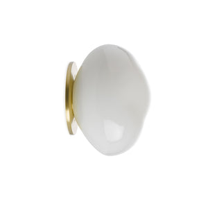 Hadeland Glassverk Crystal Stone vegglampe i hvitt glass, håndblåst med organisk form, festet til gullfarget veggplate, ideell for stemningsbelysning.