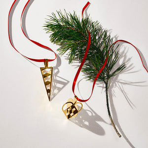 Georg Jensen julehjerte 2025 sammen med geometrisk ornament, begge i 18 karat gullbelagt messing, hengende fra rødt silkebånd.