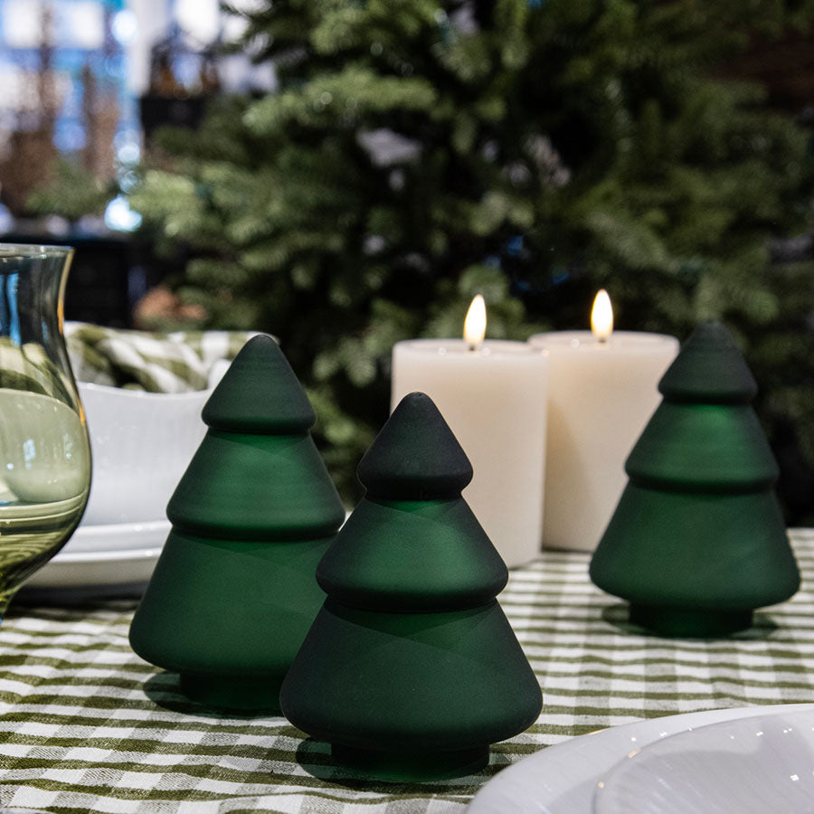 Tre frostede grønne juletrær i glass fra Hadeland Glassverk plassert på et festdekket bord med stearinlys, perfekt for julefeiring.