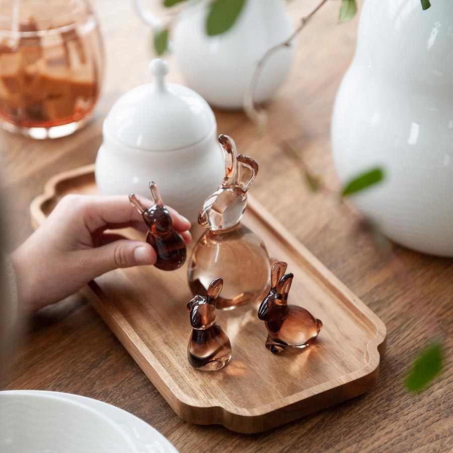 En hånd plukker opp en av de små glassharene fra et trekket på en borddekorasjon med flere glassfigurer.