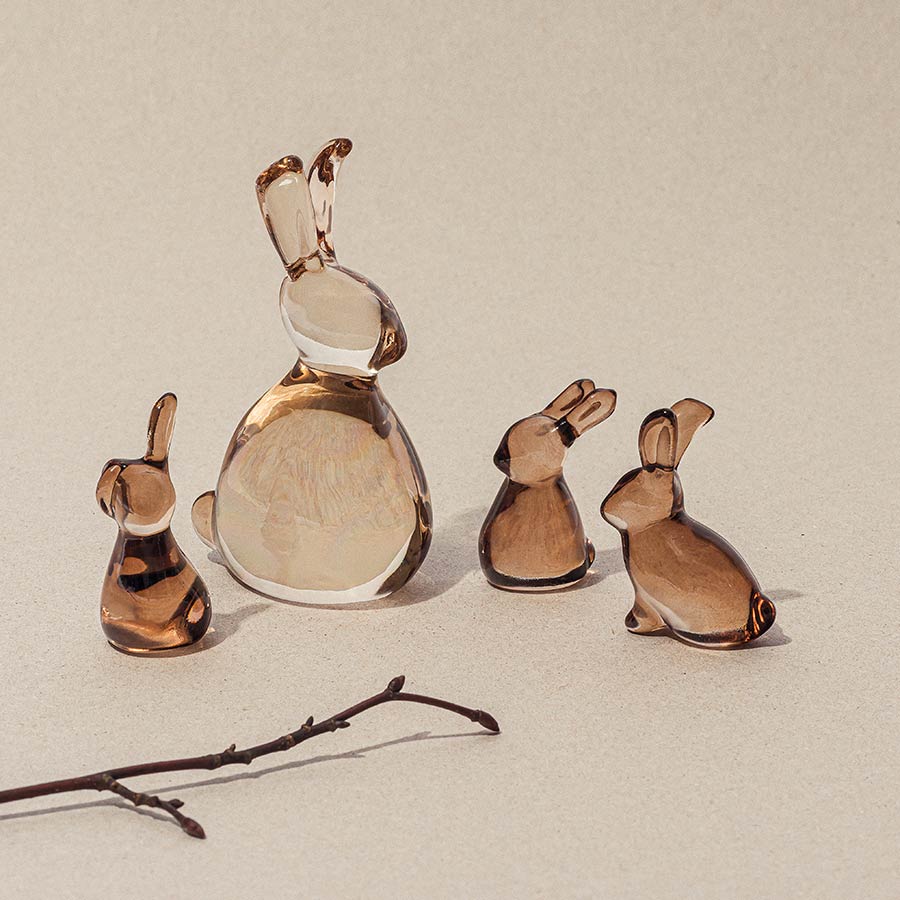 Gruppere med glassharer i ulike høyder, med en stor hare i midten, plassert på en beige bakgrunn.