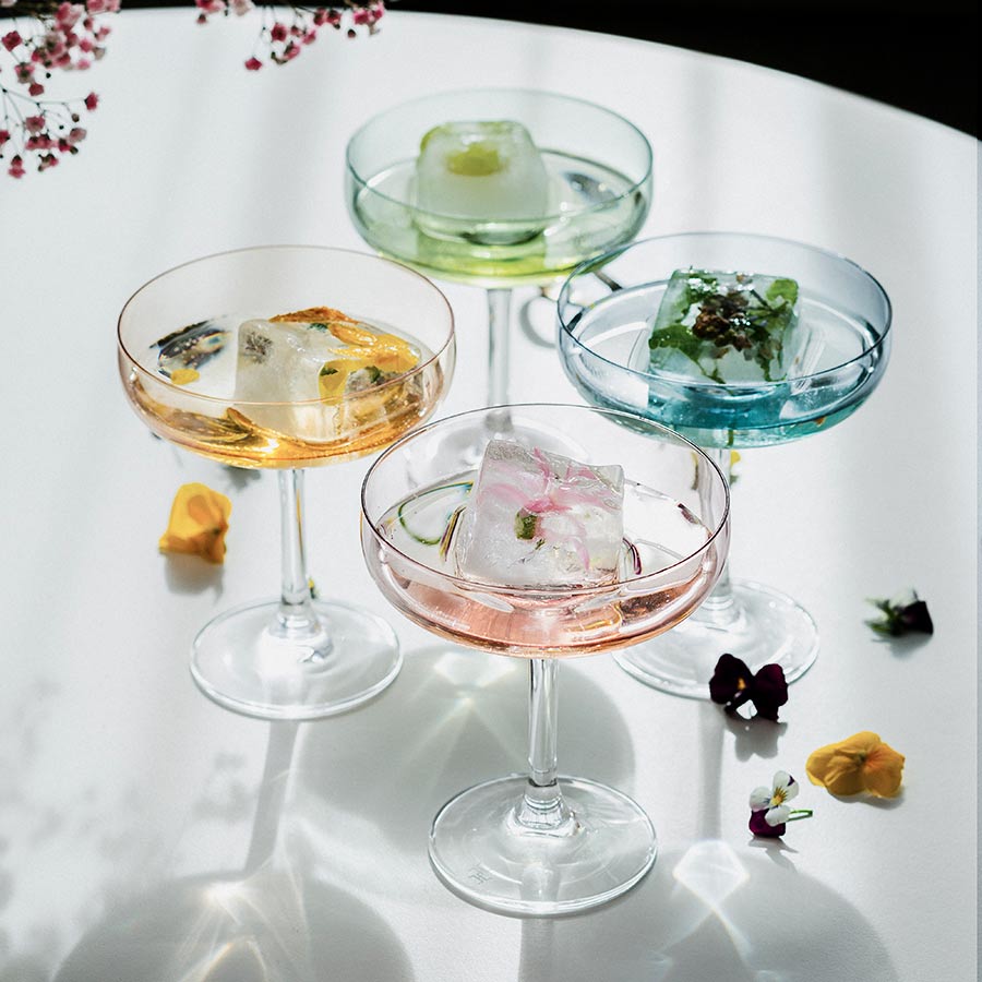 Hadeland Glassverk Odyssé Cavaskål Orange 25cl, et sett med fire fargerike glass fylt med is og dekorative blomster, ideelt for festlige anledninger.
