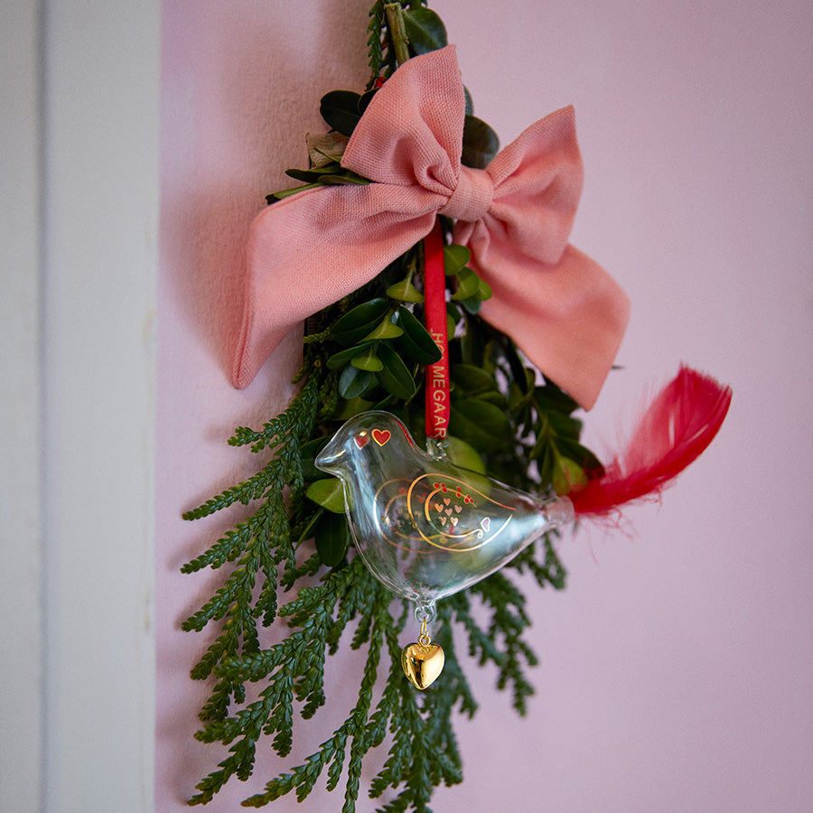 Holmegaard julefugl hengende fra en krans, munnblåst glassdekorasjon med rødt silkebånd og gullhjerte, ideell for juledekor.