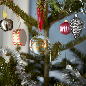 Holmegaard julekule hengende på juletreet, omringet av skinnende julepynt, visualiserer julestemning med elegant design av Ann-Sofi Romme.