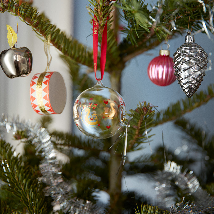 Holmegaard julekule hengende på juletreet, omringet av skinnende julepynt, visualiserer julestemning med elegant design av Ann-Sofi Romme.