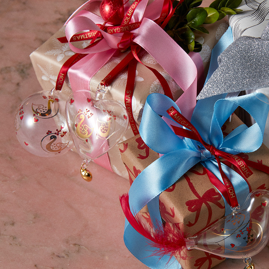Holmegaard julekule kombinert med gaver, dekorert med bånd i rosa og rødt, fremhever den klassiske julestilen designet av Ann-Sofi Romme.