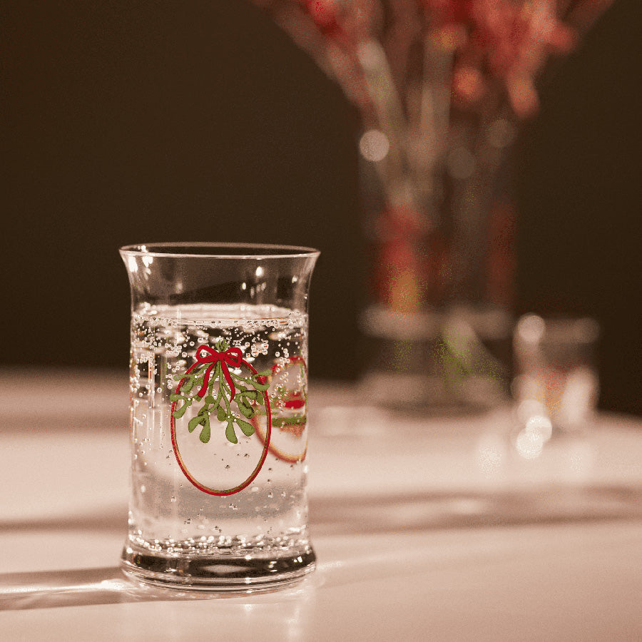 Julevannglass fra Holmegaard med sprudlende drikke, dekorert med festlige julebånd og misteltein.