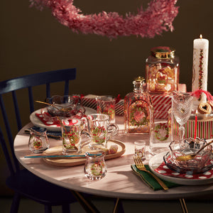 Stemningsfylt juledekorasjon på et bord, inkludert Holmegaard julelyslykter designet av Jette Frölich, glass med julemønster, julegaver og festlig oppdekking. Perfekt for å skape en romantisk atmosfære i juletiden.