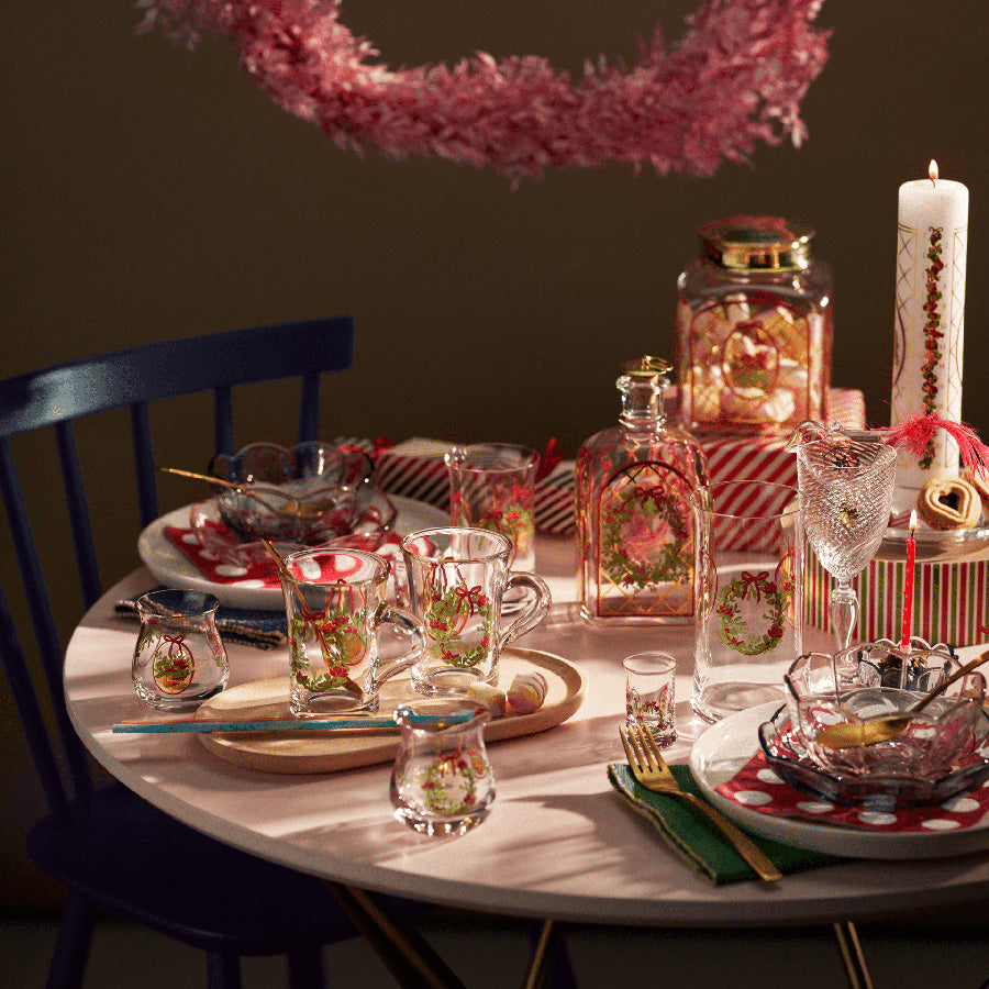 Stemningsfylt juledekorasjon på et bord, inkludert Holmegaard julelyslykter designet av Jette Frölich, glass med julemønster, julegaver og festlig oppdekking. Perfekt for å skape en romantisk atmosfære i juletiden.