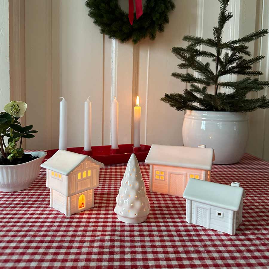Koselig julerom med Porsgrunds Porselænsfabrik Jul på Tunet Juletre Telysholder 11 cm og flere porselenshus, omringet av juledekorasjoner.
