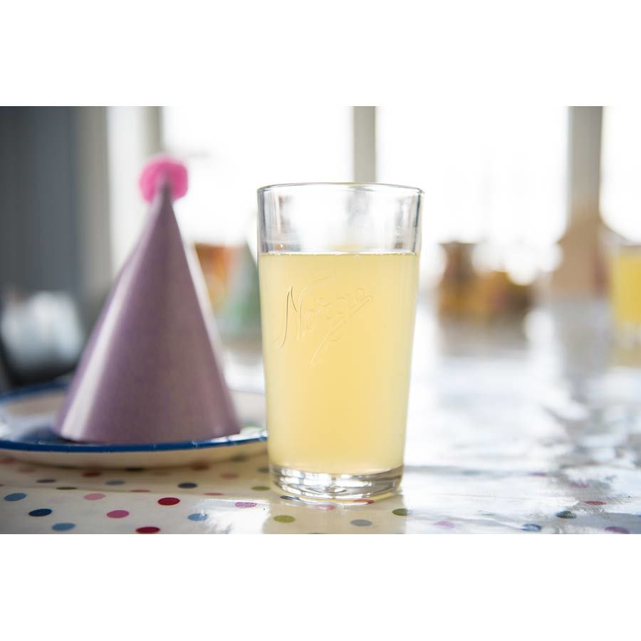 Norgesglasset drikkeglass 400ml fylt med en lys drink, ved siden av et festlig kronen på et bord.