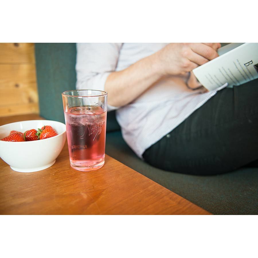Norgesglasset drikkeglass 400ml i bruk, fylt med en kjølig rosa drink på en sofa med en bolle friske jordbær.