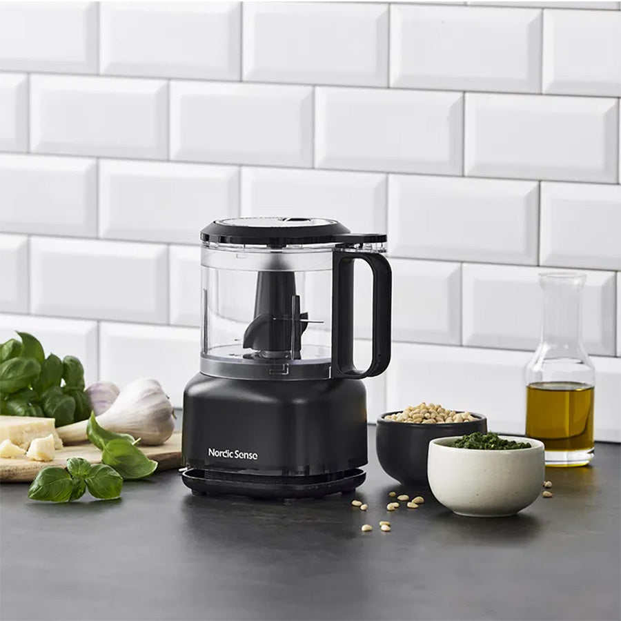 Nordic Sense minihakker i bruk på et kjøkken, med grønne urter og ingredienser rundt. Ideell for å lage sauser og pesto.