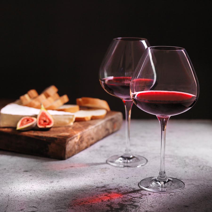 Hadeland Glassverk Odyssé Rødvin Glass 82cl 6pk - To rødvinsglass fylt med vin, servert med ost og kjeks på et bord, ideelt for underholdning.