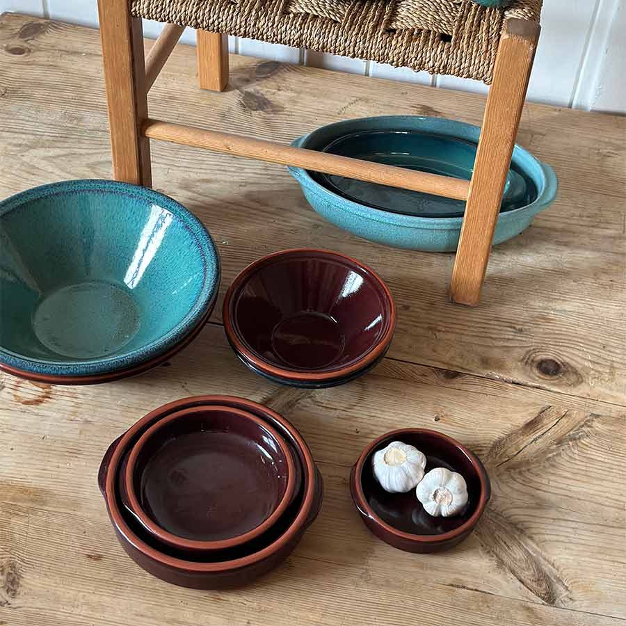 Porsgrunds Porselænsfabrik Terra serveringsbolle 38cm Verde plassert ved siden av mindre terrakottaboller, fylt med hvitløk, på et trebord.