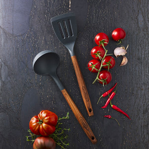 Scanpan Serveringsskje 31cm Karbonisert Ask, sammen med slikkepott og tomater, fremhever det naturlige materialet og designet for matlaging.