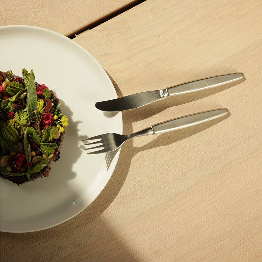 Skaugum bestikksett på en tallerken med en fargerik rett. Viser det stilige og funksjonelle designet til bestikksettet.