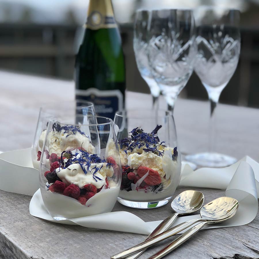 To vannglass fra HADELAND GLASSVERK fylt med friske bær og krem, servert med champagneglass.