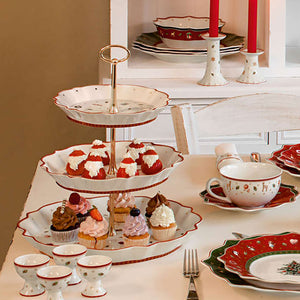 Villeroy & Boch Toys Delight etasjefat på festbord, fylt med cupcakes og delikate julekaker, sammen med julepyntede tallerkener.