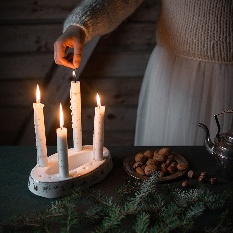 En hånd tenner et lys på Wik & Walsøe Julemorgen Story adventsstake, med en varm og hyggefylt atmosfære.