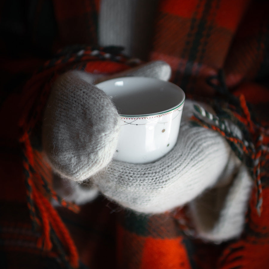 Nærbilde av Julemorgen julekopp fra WIK & WALSØE i en hånd med varme votter, ideell for servering av desemberdrikker.