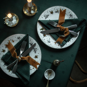 En stemningsfull borddekkingsscene med Wik & Walsøe Julemorgen servietter, dyp grønn farge, kombinerte med keramiske tallerkener og dekorative detaljer.