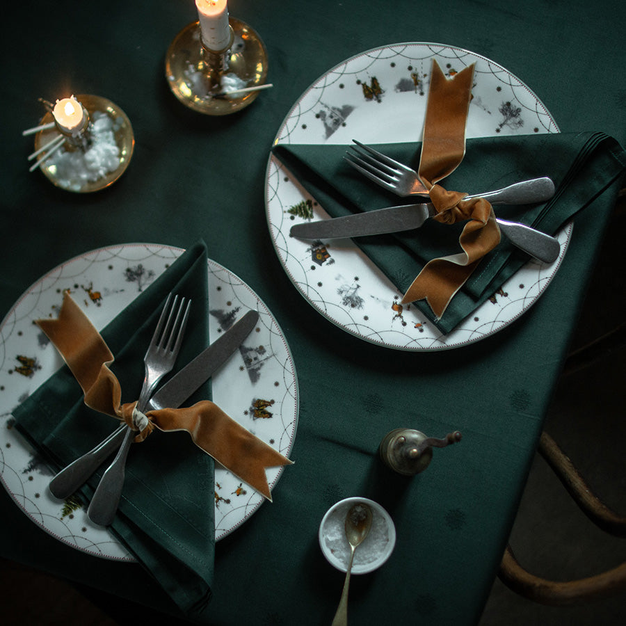 En stemningsfull borddekkingsscene med Wik & Walsøe Julemorgen servietter, dyp grønn farge, kombinerte med keramiske tallerkener og dekorative detaljer.
