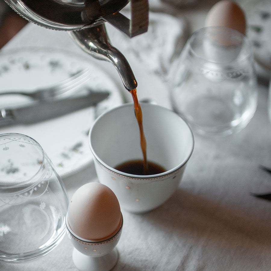 Kaffe helles i en elegant julekopp fra Wik & Walsøe, plassert på bordet med et egg og dekorative tallerkener, perfekt for førjulsfin mat.