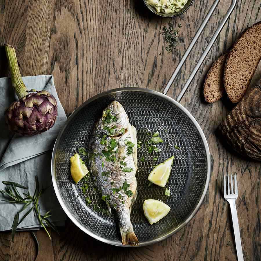 Rettferdig tilberedt fisk med sitron og urter i en keramisk stekepanne på en treskjærebrett, perfekt for matlaging med stekepanne.