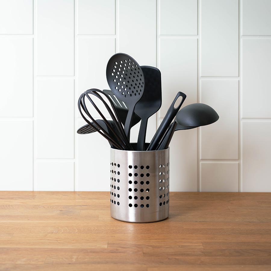 Kjøkkenredskaper i en stilren beholder i rustfritt stål, inkludert visper, skjeer og spatler, perfekt for et moderne kjøkken.