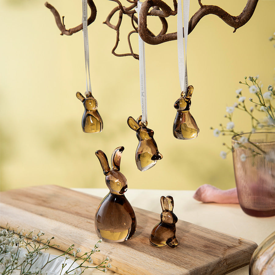 Elegant påskepynt fra Hadeland Glassverk, inkludert søte glassharer og fargerike glassegg, plassert på et bord med en naturlig gren som gir en vårstemning.