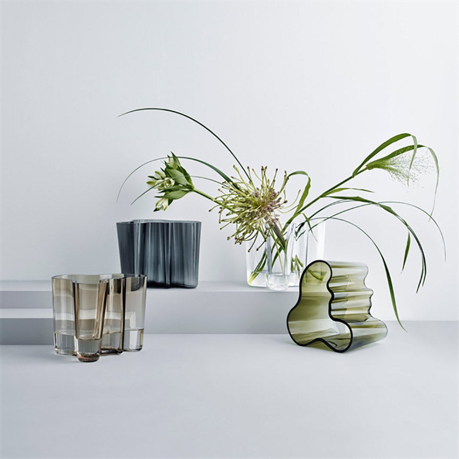 Stilrene Iittala vaser og glass i forskjellige farger, plassert på en lys grå overflate, med dekorative blomster. Perfekt for skandinavisk interiørdesign.