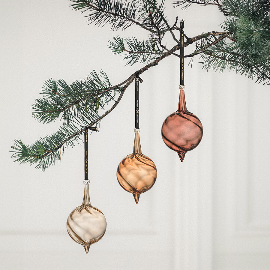 Elegante juletrepynt i glass i tre forskjellige farger henger fra en juletregren, perfekt for å dekorere julen.