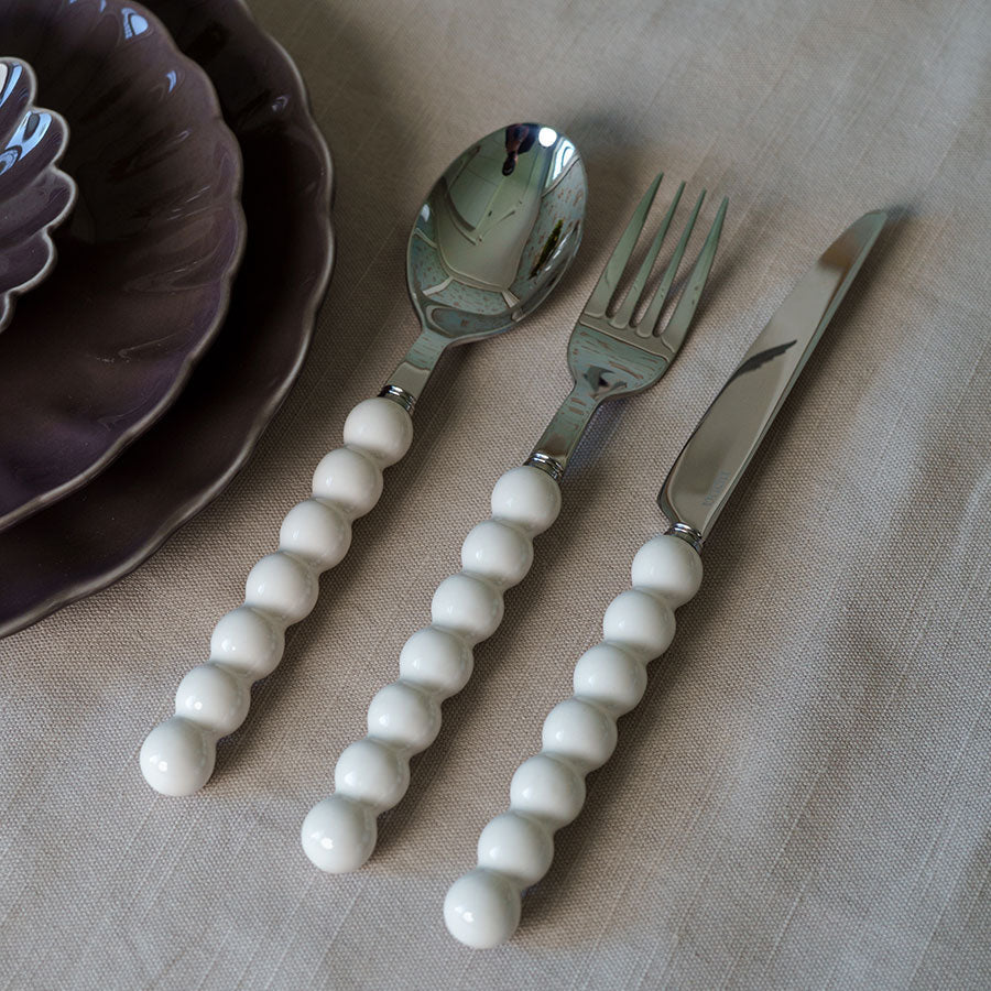 Elegant bestikksett med hvite, perleformede håndtak. Inkluderer skje, gaffel og kniv, perfekt for stilige middager og hverdagsbruk.