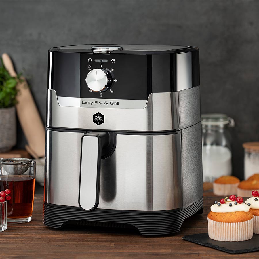 OBH Nordica Easy Fry & Grill Classic+ 2in1 airfryer i sølv, plassert på et kjøkkenbord med ingredienser og bakverk rundt, perfekt for sunn steking og grilling.