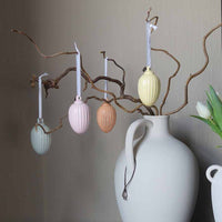 Dekorative påskeegg i pastellfarger henger fra grener i en vase, og gir en vakker påskedekorasjon i moderne stil.