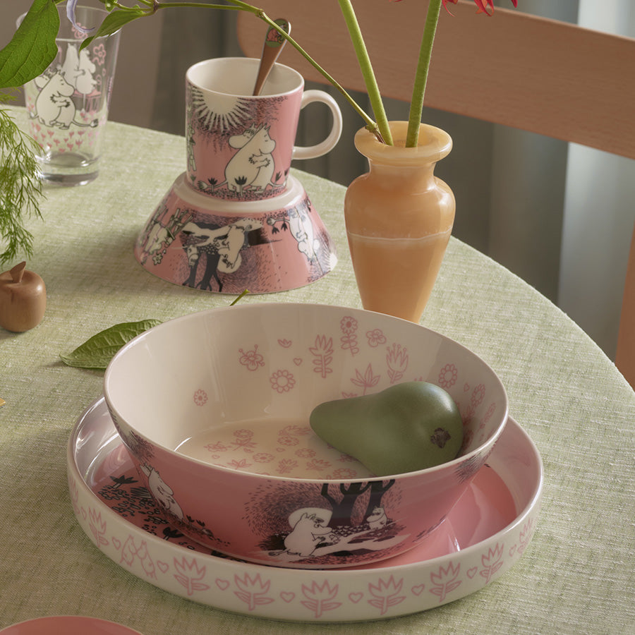 Moomin Arabia serveringsskål plassert på et bord med matchende Mumin-varer, dekorativt med erter og blomstermotiv.