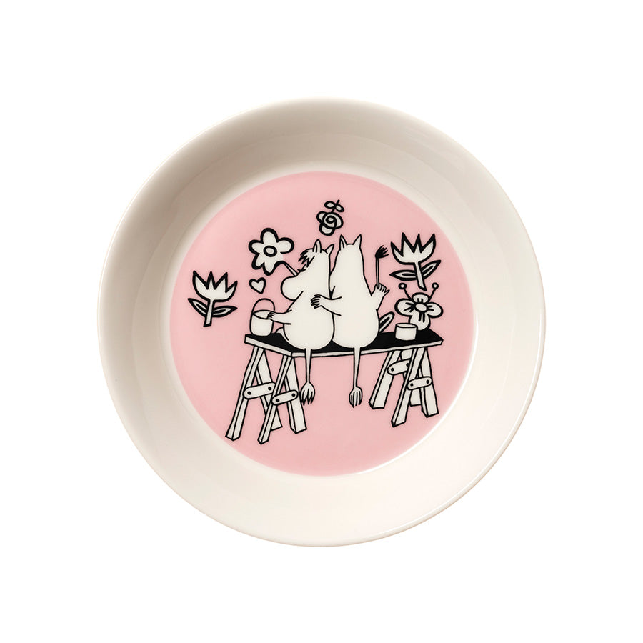 Moomin Arabia asjett med rosa bunn og illustrasjon av Mummitrollet og Snorkfrøken som sitter sammen ved et bord med blomster. Ideell til servering av småretter.