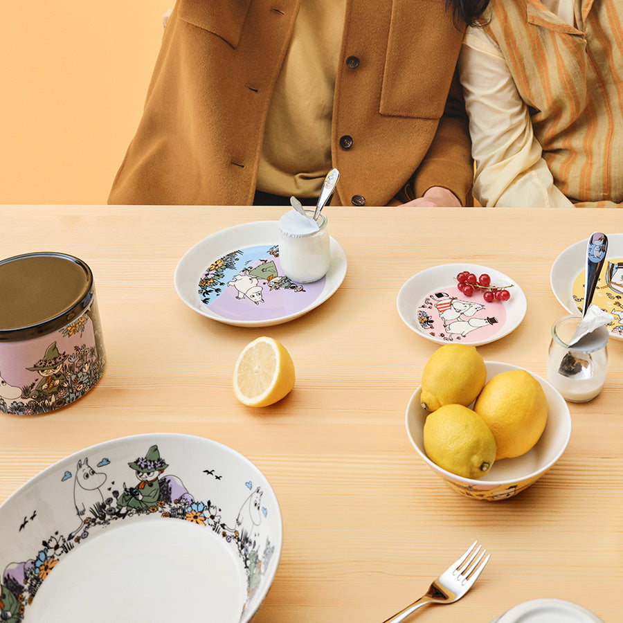 Bordoppsett med Moomin serveringsskål, småretter og frukt, som skaper en innbydende atmosfære for samvær.